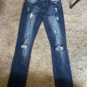 Mörkblå skinny jeans från Sheilay - Snygga mörkblå skinny jeans från Sheilay med slitna detaljer och hål på knäna. Jeansen har klassisk femficksdesign, normal midja och är tillverkade i stretchigt denim för en tight passform. Perfekta för en trendig och avslappnad look.