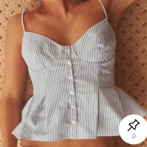 Randig korsettopp med knappar - Säljer en snygg randig korsettopp med smala axelband och knappar framtill. Toppen har en figurnära passform upptill och en lätt utsvängd nederdel. Perfekt för varma dagar! Helt ny med lappen kvar! Säljes för att den tyvärr var för liten..