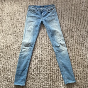 Ljusblå skinny jeans från Replay - Säljer ett par ljusblå skinny jeans från Replay, modell LUZ. Jeansen har klassisk femficksdesign, låg midja och är tillverkade i stretchig denim för en tight passform. Perfekta för dig som gillar en smal siluett och vill ha en fräsch, ljus tvätt.