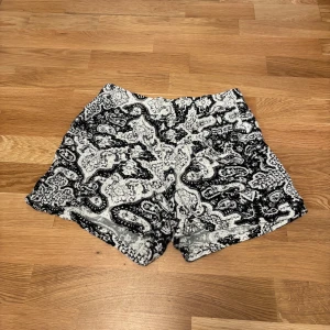 Svartvita mönstrade shorts med fickor KappAhl - Snygga svartvita shorts med 2 fickor på framsidan från KappAhl i storlek S. De har ett unikt paisleymönster och är tillverkade i mjuk bomull. Modellen är loose fit med elastisk midja för extra komfort. Perfekta för varma sommardagar när du vill sticka ut lite extra.
