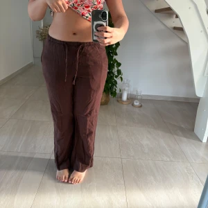 Bruna linnebyxor  - Säljer ett par bruna linnebyxor med avslappnad passform och dragsko i midjan. Perfekta för varma dagar och har en enkel, stilren look. Byxorna har raka ben och resår i midjan för extra komfort. Säljs då det är lite kortare på mig med skor. Jag är ungefär 167