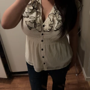 Vit prickig blus med volang - Supersöt vit blus med små svarta prickar och volangdetaljer längs v-ringningen. Knappar framtill och lätt rynkad midja. Passar mig som vanligtvis har M💕