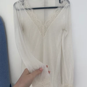 Intimissimi topp - Säljer en vit långärmad Intimissimi topp med v-ringning och fina spetsdetaljer vid halsringning och ärmslut. Tunn och mjuk, perfekt att styla lager på lager eller som den är. Enkel men ändå elegant look.