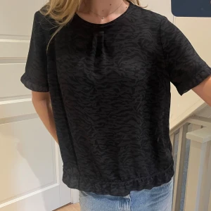 Svart blus - Snygg svart skjorta från 365 med diskret zebramönster. Blusen har korta ärmar, knappar baktill, men kan även has fram och en avslappnad passform. Perfekt till jeans. Den är i storlek 40 men passar S/M, jag har 36/38 och S. 