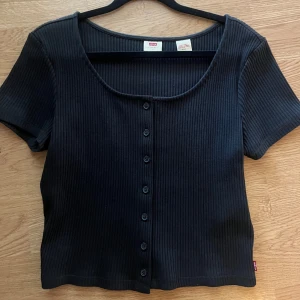 Svart topp från Levi's - Säljer en svart classy topp från Levi's med korta ärmar och knappar framtill. Supersnygg och knappt använd i mycket bra skick och alla lappar kvar. Storlek M 