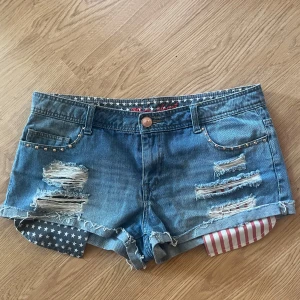 Världens snyggaste jeansshorts  - Säljer ett par vintage lowwaist jeansshorts med skitsnygga detaljer på fickorna och slitningar i USA tema. De är ifrån märket mini short och är i storlek 42, men är egentligen mindre i storleken då den är vintage, passar bra för någon i storlek 40, och 38 också! 