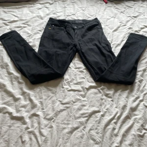 Tiger of Sweden jeans slim fit - Svarta jeansbyxor med slim passform och klassisk femficksdesign. Byxorna har dragkedja och knapp framtill samt bälteshällor. Passar perfekt till en stilren och enkel look.