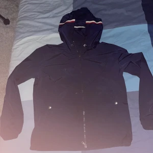 Moncler windbreaker  - Snygg mörkblå moncler vindjacka med huva och dragsko. Jackan har dragkedja framtill och två fickor med knappar. Perfekt för blåsiga dagar och enkel att matcha med olika outfits. Enda problemet e att zipen har gått sönder men går att fortfarande zipa up o ner den som vanligt:)