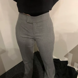 Grå kostymbyxor med hög midja - Snygga grå kostymbyxor med hög midja och rak passform. Byxorna har en stilren look utan synliga detaljer framtill och är perfekta för en clean och klassisk stil.