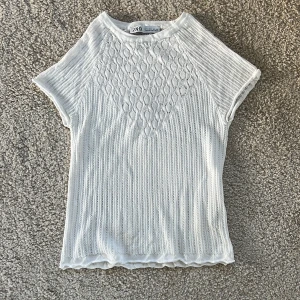 Vit stickad topp från Zara - Säljer en söt vit stickad topp från Zara med korta ärmar och fint hålmönster. Toppen har rund halsringning, tröjan är tunn vilket ger en luftig känsla.  De är storlek L men den passar även S
