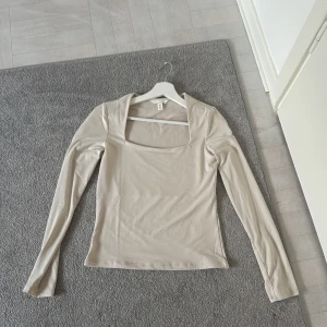 Beige långärmad topp med fyrkantig ringning från H&M - Säljer en beige långärmad topp från H&M med snygg fyrkantig ringning. Toppen är i ett mjukt och stretchigt material och har en tight passform. Perfekt att styla med jeans eller kjol för en clean look.