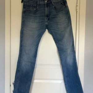 Replay jeans - Säljer ett par Replay Anbass jeans i klassisk blå denim. Jeansen har normal passform, raka ben och fem fickor. Snygga slitningar och Replay-logga på bakfickan. Perfekta för en avslappnad stil.