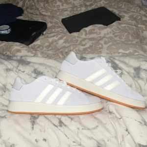 Vita sneakers från Adidas med gummisula - Hel nya skor som är köpte idag men säljer pågrund av att det var för små orginalpris 1300. Fräscha vita sneakers från Adidas med klassiska tre ränder på sidan och ljusbrun gummisula. Skorna har snörning och en låg profil, perfekt för en clean och sportig look.