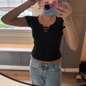 Svart ribbad croppad topp med snörning - Säljer en svart croppad topp från lager 157 i The Black Label Collection. Toppen är ribbad och har snörning framtill vid urringningen. Perfekt till jeans eller kjol för en trendig look.