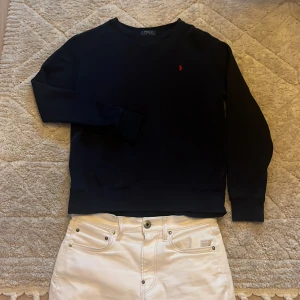 Mörkblå sweatshirt från Polo Ralph Lauren - Säljer en klassisk mörkblå sweatshirt från Polo Ralph Lauren med den ikoniska röda loggan broderad på bröstet. Tröjan har rund halsringning och långa ärmar. Perfekt för en stilren och avslappnad look.