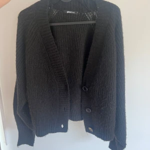 Svart stickad kofta från Gina Tricot - Mysig svart stickad kofta från Gina Tricot med djup v-ringning och stora knappar framtill. Koftan har långa ärmar och en lite lösare passform, perfekt att slänga på sig över en topp. Aldrig använd🤍