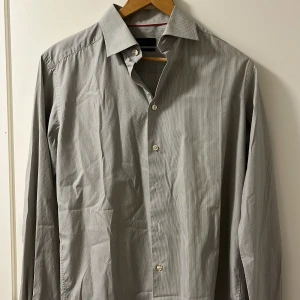 Gråvit randig skjorta från Eton - Säljer en stilren gråvit skjorta från Eton i slim fit-modell. Skjortan har tunna ränder, klassisk krage och vita knappar. Perfekt för dig som gillar en clean och tidlös look.