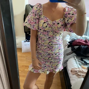 Blommig miniklänning - Supersöt kortklänning med blommigt mönster. Klänningen har puffiga korta ärmar, markerad midja och volang nertill. Perfekt för sommarens alla tillfällen!