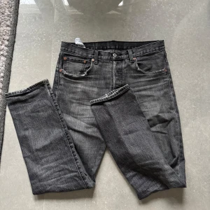 Grå jeansbyxor Levis 501 - Säljer ett par klassiska grå Levis 501 jeans med raka ben och femficksdesign. Byxorna har knappgylf och är i en snygg tvättad grå färg. Perfekta för dig som gillar tidlös stil och vill ha ett par jeans som funkar till allt. Byxorna är ganska slitna men går fortfarande att använda!
