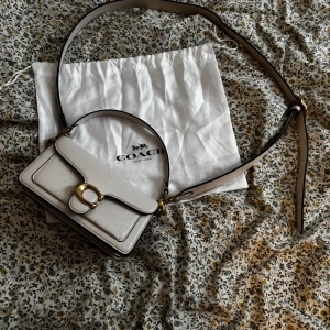 Coach Tabby 20 axelväska  - Coach Tabby axelväska i ljusbeige skinn med guldfärgade metalldetaljer och klassiskt C-spänne. H- 11cm L- 20cm B-7cm