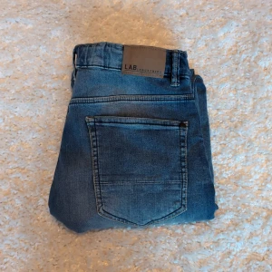 Blå jeans från LAB Industries - Snygga blå jeans från LAB Industries med slitningar på benen och klassisk femficksdesign. Jeansen har normal passform och är tillverkade i denim med en lätt tvättad look. Perfekta för en avslappnad stil.