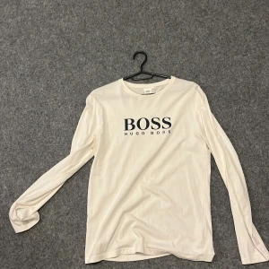 Vit långärmad tröja från Hugo Boss - Snygg vit långärmad tröja från Hugo Boss med stor svart logga framtill. Tröjan har rund halsringning och är gjord i mjuk bomull, perfekt för en clean och stilren look. Passar dig som gillar klassiska och enkla plagg med premiumkänsla. Pris går att diskuteras storleken passar bra till s och precis så att den passar till M