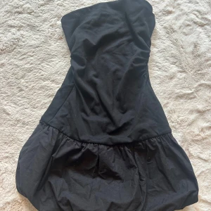 Svart axelbandslös klänning - Snygg svart kort axelbandslös klänning från Bershka med puffig kjol. Har tyvärr aldrig fått användning för den, så den är som helt ny!