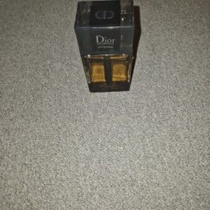 Dior Homme Intense Eau de Parfum - Lyxig herrparfym från Dior, Homme Intense. Flaskan är rektangulär med svart lock och transparent glas som visar den gyllene vätskan inuti. Perfekt för dig som gillar eleganta och sofistikerade dofter.