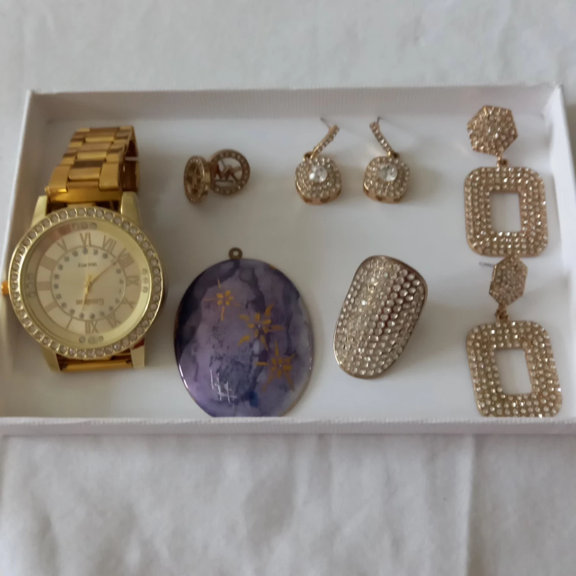 Mix av smycken och klocka i guld och lila