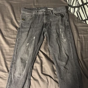 Grå jeans Tiger of Sweden Pistolero - Snygga grå jeans från Tiger of Sweden i modellen Pistolero. Jeansen har en tvättad look med slitningar och raka ben. Färgen är mercury gray och materialet är klassisk denim. Perfekta för dig som gillar en avslappnad men stilren vibe.