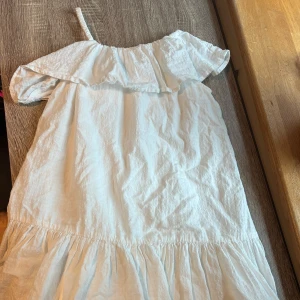 Vit offshoulder barnklänning Kappahl storlek 134 - Superfin vit kortklänning från Kappahl i bomull med volang upptill och offshoulder-design. Klänningen har en axelbandslös look med en smal axelrem och rynkad nederdel som ger en luftig känsla. 