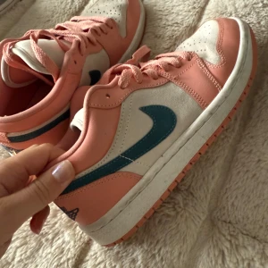 Nike sneakers i rosa och vitt med blå swoosh - Säljer ett par Nike sneakers i låg modell med rosa och vita paneler samt blå swoosh på sidorna. Skorna har snörning och rund tå. Perfekta för dig som vill ha en färgglad och sportig look. Nypris 5000kr från Dubai!