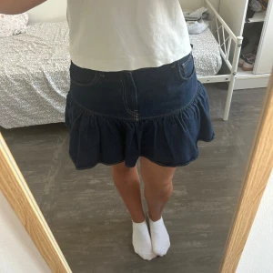 Mörkblå volangkjol i jeans - Supersöt mörkblå jeanskjol med volang och markerad söm. Kjolen har väldigt liten i storleken.