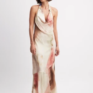 Långklänning i satin med akvarellmönster - Säljer en elegant långklänning i satin med halterneck och öppen rygg. Klänningen har ett akvarellmönster i ljusa toner av beige, rosa, blått och rött. Snygg drapering framtill och knyt i nacken. Perfekt för sommarens tillfällen! Storlek xs (34), enbart använd vid ett tillfälle 🩷
