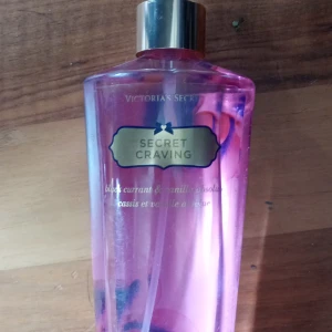 Victoria's Secret Secret Craving mist - Fräsch och söt body mist från Victoria's Secret i doften Secret Craving. Flaskan är genomskinlig med rosa vätska och har ett guldigt lock. Doften har inslag av svartvinbär och vanilj. Rymmer 250 ml och är perfekt för dig som gillar fruktiga och söta toner.