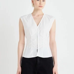 Vit randig  v-ringad blus - Snygg vit randiga blus med v-ringning och markerad midja. Ärmlös design och stilren passform som ger en elegant siluett. Perfekt att matcha med både kjol och byxor för en trendig look.