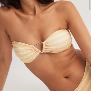 Randig bandeau bikiniöverdel - Söt bandeau bikiniöverdel med pastellfärgade ränder i gult, rosa och vitt. Toppen har en dekorativ metallring framtill och avtagbara axelband. Perfekt för sommaren. Endast testad och säljs för att storleken var fel för mig. Storlek M men passar s-m mer skulle jag säga💞💞💞