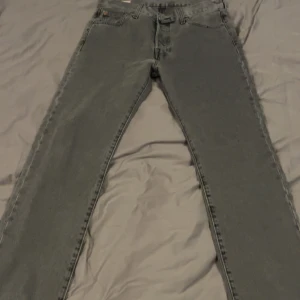 Grå Levi's 501 jeans - Säljer ett par klassiska grå Levi's 501 jeans med raka ben och knäppning fram. Byxorna har fem fickor och den ikoniska läderpatchen bak i midjan. Perfekta för dig som gillar tidlös denimstil. Aldrig använda 