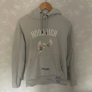 Grå hoodie från Hoodrich med duvor - Snygg ljusgrå hoodie från Hoodrich med tryck av två duvor framtill och stor duva med texten 'From Nothing To Something' på ryggen. Tröjan har huva med snörning och magficka. Perfekt för dig som gillar streetwear vibes.