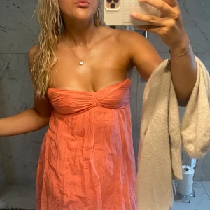 Axelbandslös korallrosa kortklänning - Superfin axelbandslös kort klänning i en härlig korallrosa färg. Lätt och luftig modell med twistad detalj vid bysten och rynkad kjol. Perfekt för varma dagar och sommarvibbar. Materialet känns tunt och svalt, linne. har tyvärr några skador de sista bilden🩷