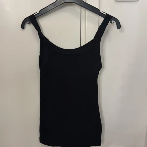 Svart ribbad linnetopp från H&M XS - En svart ribbad linnetopp från H&M i storlek XS. Toppen har smala axelband och ärmlös design, perfekt för lager-på-lager eller att bära som den är. Enkel och stilren modell som funkar till många olika looks.