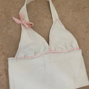 Topp - Egensydd supersöt jeans halterneck med svarta knappar i ryggen. Ljusrosa sömmaar samt en ljusrosa roset på ena axelbandet.