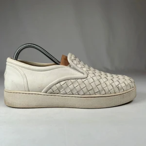 Vita slip-on sneakers i flätat skinn - Snygga vita slip-on sneakers med flätad ovandel i skinn. Skorna har en platt sula och rund tå, vilket ger en clean och stilren look. Perfekta för dig som gillar minimalistisk design med en twist. Passar till det mesta och är superenkla att dra på sig.