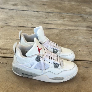 Nike Air Jordan 4 White oreo 42 - Nike Air Jordan 4 White Cement med vit ovandel i skinn, grå detaljer med svart stänkmönster och röda Jumpman-loggor på plösen. Klassisk siluett med meshpaneler, snörning och robust sula. Perfekta för dig som vill sticka ut med en ikonisk sneaker.