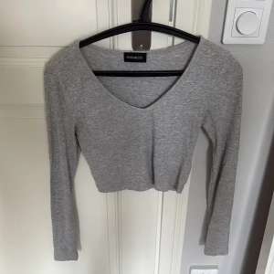 Grå croppad långärmad topp Even&Odd - Säljer en ljusgrå croppad topp från Even&Odd med v-ringning och långa ärmar. Toppen är ribbad och har en slim passform som sitter snyggt på kroppen. 🩶