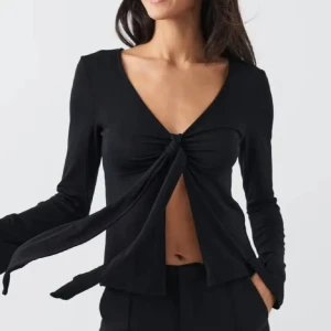 Svart långärmad omlottopp med knyt - Trendig svart långärmad topp från Gina Tricot med djup v-ringning och knyt framtill. Toppen har croppad passform och långa band som ger en snygg omlottkänsla. Perfekt för dig som gillar stilrena och coola plagg med det lilla extra.
