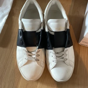 Valentino Garavani Open svart/vit - Snygga Valentino Garavani Open skori storlek 44, skorna har vitt skinn med bred svart läderdetalj över snörningen. Klassisk rund tå, platt sula och diskreta nitar baktill. Kommer med originalkartong, dustbag och påse. Perfekta för dig som gillar lyxiga skor. Priset kan diskuteras vid snabb affär