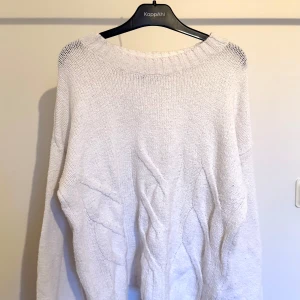 Vit stickad tröja - Mysig vit tröja med grov kabelstickning framtill och bred ribbad halsringning. Tröjan har lång ärm och en relaxed fit, perfekt för lager på lager under kyliga dagar.