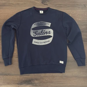 Mörkblå sweatshirt från Lee, Salina-print - Mörkblå sweatshirt från Lee i storlek M med stort vintageinspirerat Salina-tryck på bröstet. Tröjan har rund hals, ribbade muddar och är tillverkad i mjuk bomull. Perfekt för dig som gillar klassisk streetstyle med en retrovibe. OBS EJ ÄKTA