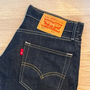 Levi's 511 jeans - Snygga Levi's 511 jeans i mörkblå denim med klassiska kontrastsömmar och röd logotagg vid bakfickan. Femficksdesign. Helt nya, oanvända.